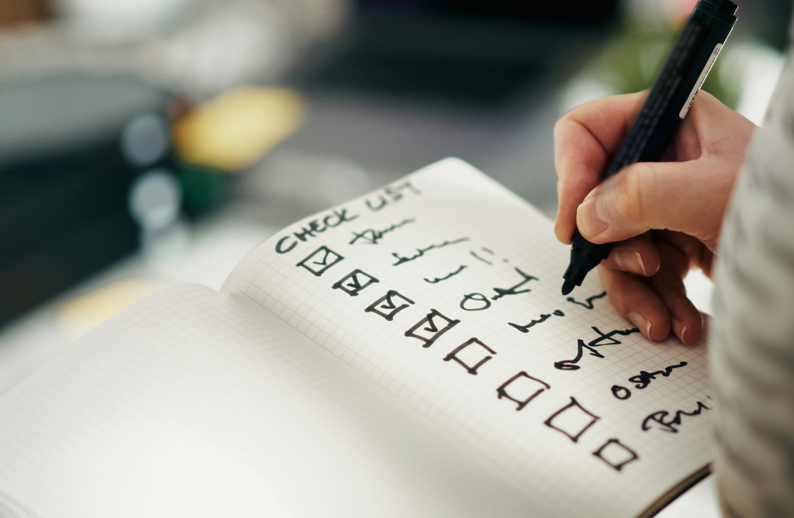 A hand ticking off completed steps in a grid notebook checklist